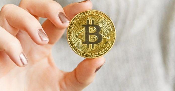 106820278-1609972654383-hand-holding-a-bitcoin-in-front-of-a-computer-screen-with-a-dark-graph-blockchain-mining-bitcoin_t20_pRrrjP